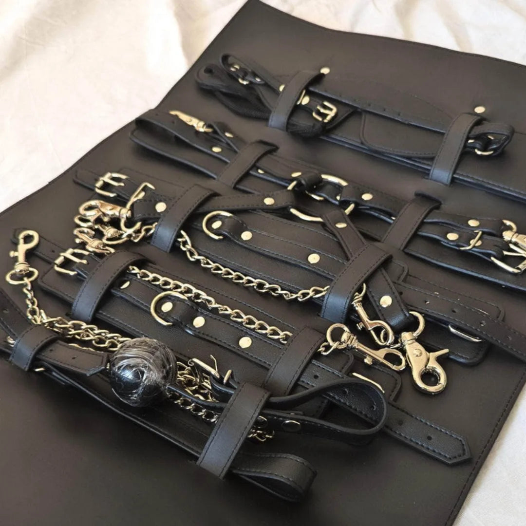 Black leather BDSM kit accessory set with gold chains and hardware on a black surface.