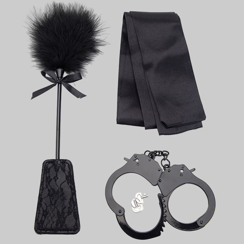 Black feather duster, black satin ribbon, and black handcuffs on a white background